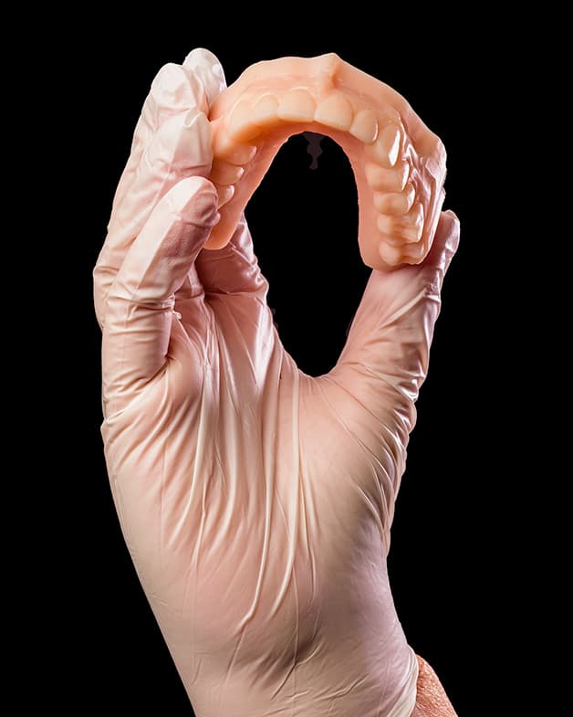 A technician pricing and making a denture at the laboratory bench